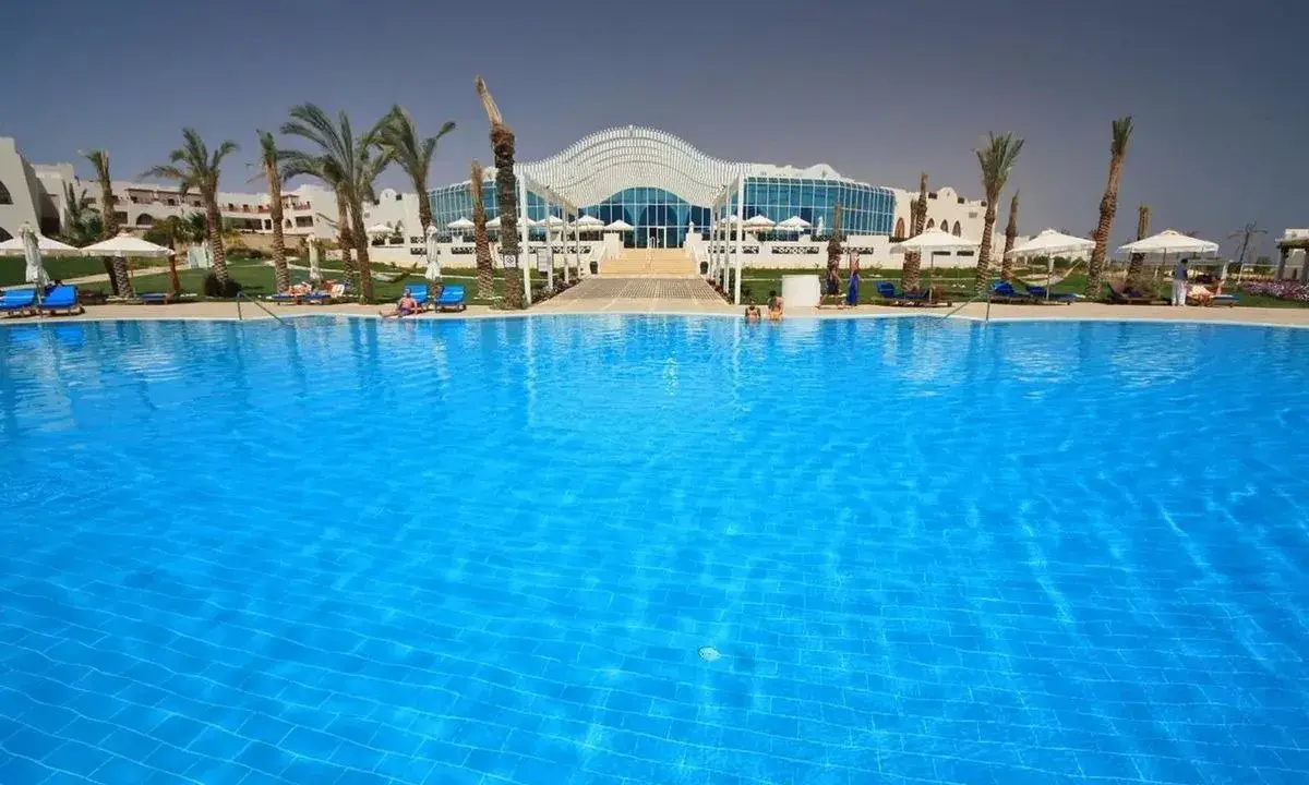Basen w Hilton Marsa Alam Nubian Resort. Wiele osób odpoczywa na leżakach pod palmami.
