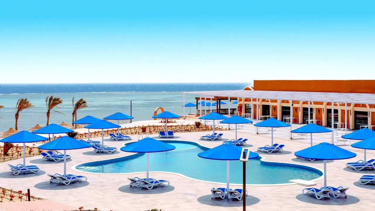 Basen z niebieskimi parasolami i leżakami, widok na morze. Idealne miejsce na wakacje, jak w Pickalbatros Portofino Marsa Alam.