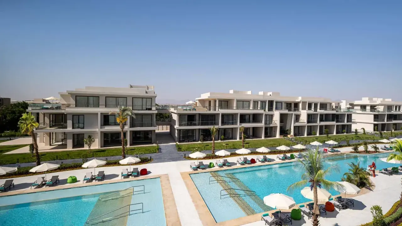 Nowoczesne budynki hotelowe Rixos z basenami i leżakami pod palmami.