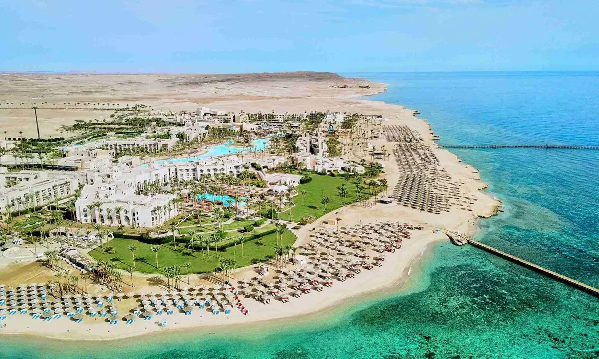 Albatros Palace Port Ghalib: rozległy kompleks hotelowy z basenami, palmami i plażą pełną leżaków, otoczony pustynnym krajobrazem i turkusowym morzem.