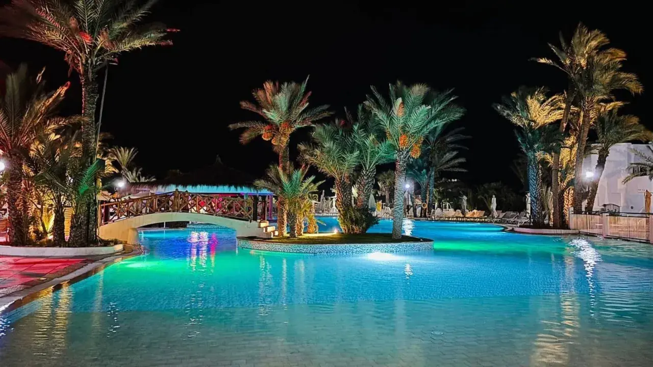 Nocny basen z palmami i mostkiem, idealne miejsce na relaks. Wiele pozytywnych fiesta beach djerba opinie potwierdza jego urok.