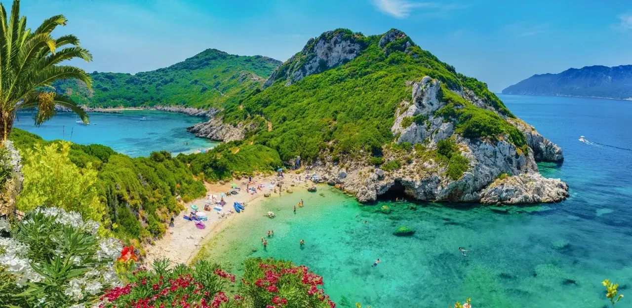 Malownicza zatoka z piaszczystą plażą, turkusową wodą, zielonymi wzgórzami i kwitnącymi kwiatami.