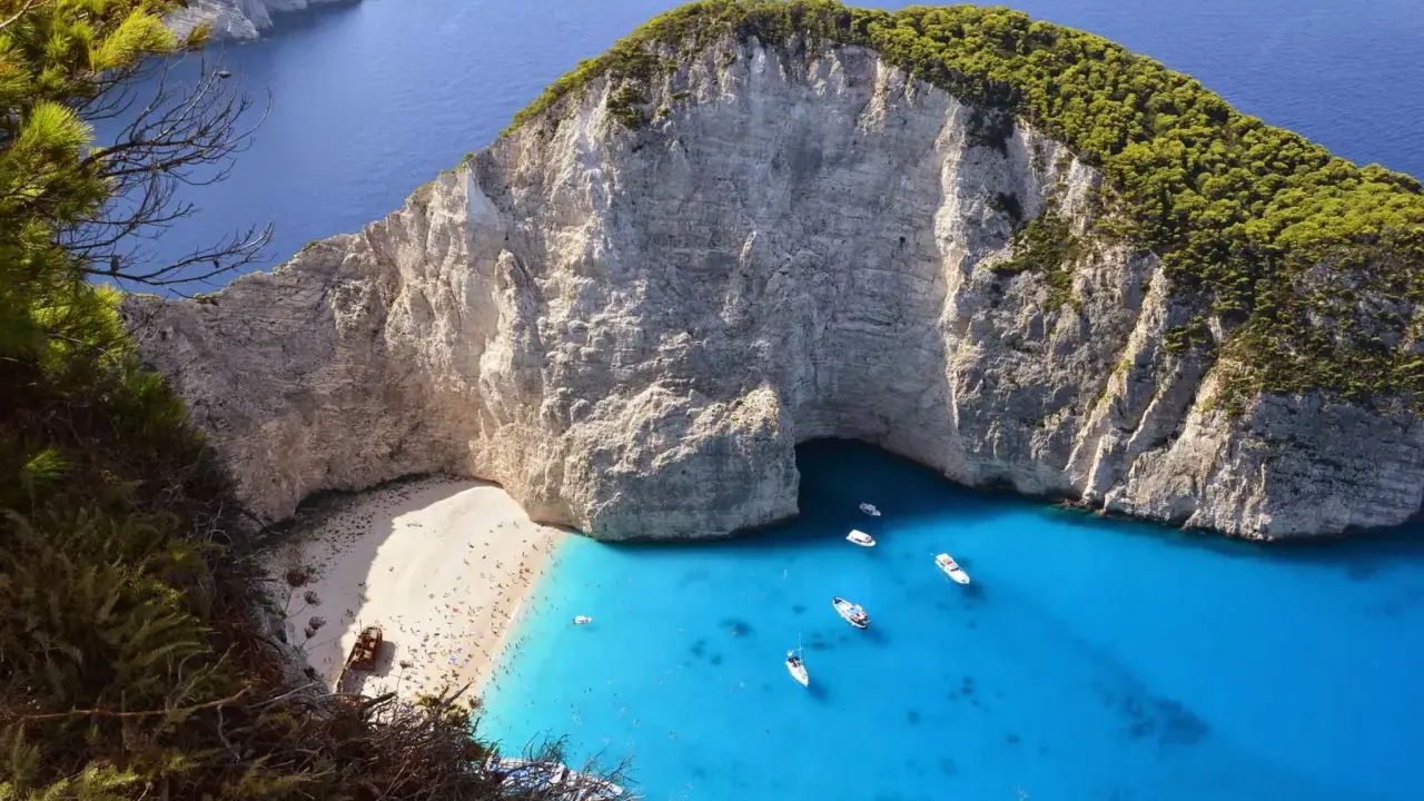 Widok na zatokę Navagio z plażą, klifami i turkusową wodą, z widocznym wrakiem statku.