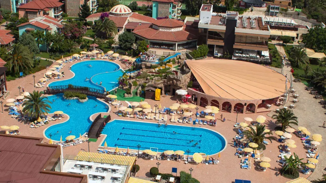 Widok z lotu ptaka na kompleks basenów i budynków hotelowych. Wiele osób odpoczywa na leżakach pod parasolami. Gypsophila holiday village opinie są pozytywne.