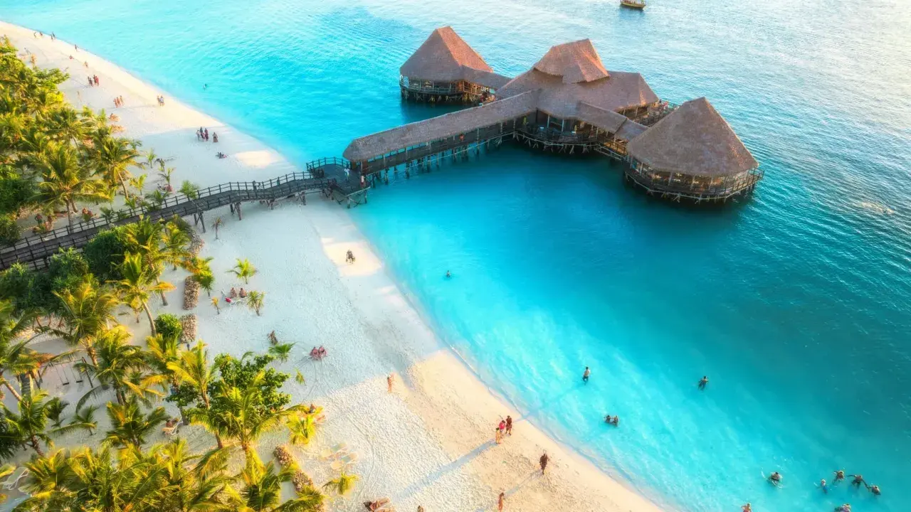 Rajska plaża na Zanzibarze z palmami i restauracją na wodzie. Sprawdź aktualne zanzibar ceny, by zaplanować wymarzone wakacje.