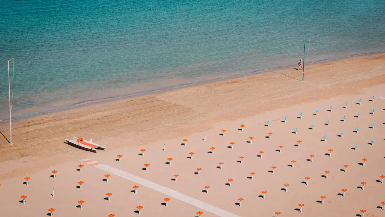 Idealne loty do Rimini: pusta plaża z rzędami parasoli, łódka na piasku i turkusowe morze.