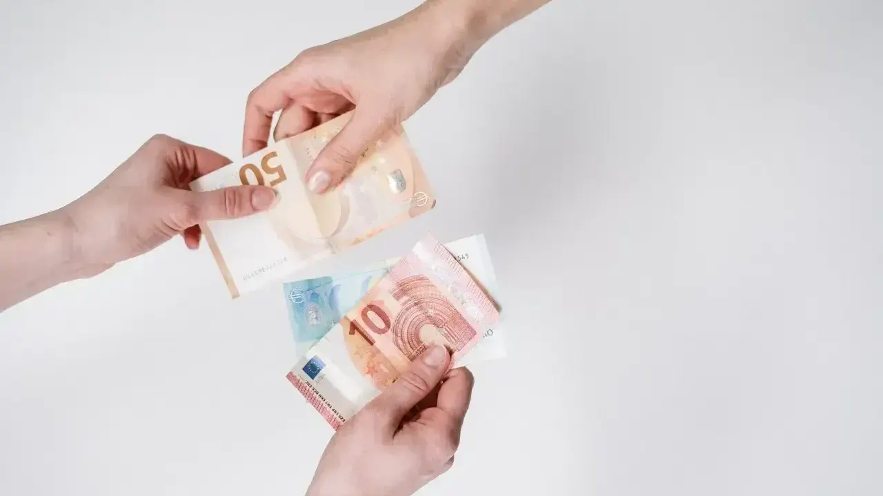 Dwie ręce przekazują sobie banknoty euro. To waluta Słowenii, używana do codziennych zakupów.