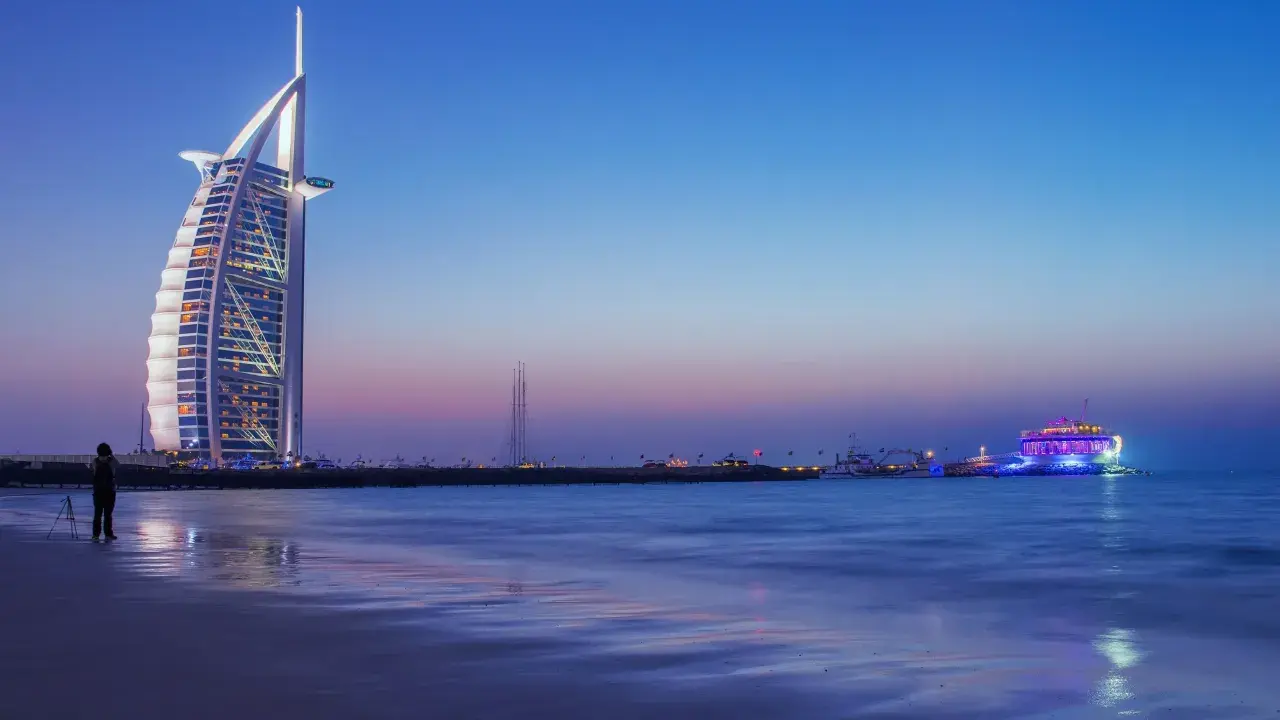Wieczór w Dubaju. Luksusowy hotel Burdż al-Arab i oświetlony statek na morzu. Ceny w Dubaju mogą być wysokie, ale widoki są niezapomniane.