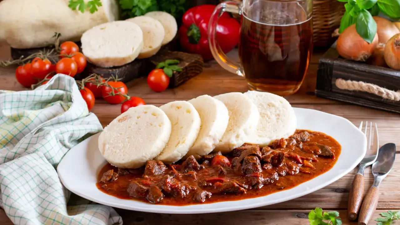 Gulasz z knedlami, piwo i warzywa na drewnianym stole.