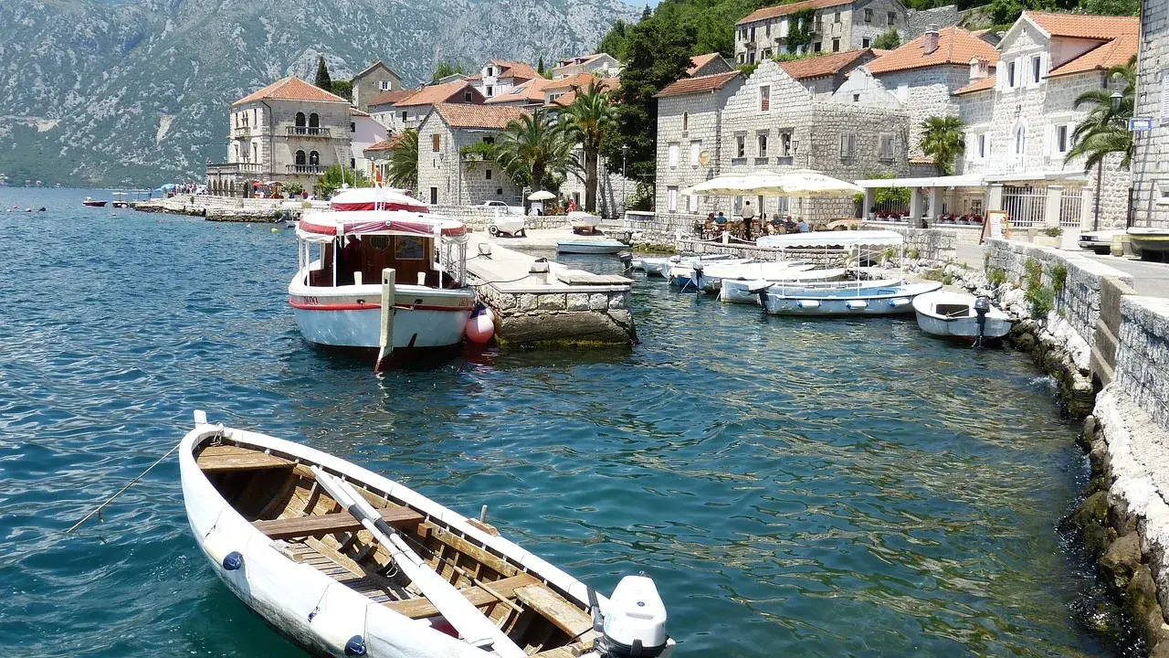 Port w Czarnogórze, łodzie na wodzie, góry w tle. Ceny rejsów mogą być różne, warto sprawdzić.