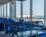 Puste, niebieskie siedzenia na lotnisku w Kalabrii, z widokiem na samolot Aegean i morze.