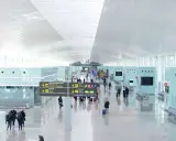 Wnętrze nowoczesnego terminalu lotniska w Hiszpanii. Pasażerowie z bagażami przemieszczają się pod jasnym, łukowatym sufitem, kierując się znakami.