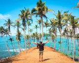 Człowiek z rozłożonymi rękami na tle palm i turkusowego oceanu. Marzysz o podróży? Sri Lanka ile trwa lot, warto sprawdzić!