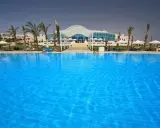 Basen w Hilton Marsa Alam Nubian Resort. Wiele osób odpoczywa na leżakach pod palmami.