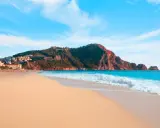 Plaża Kleopatry w Alanyi z turkusową wodą, piaszczystym brzegiem i górującym nad nią masywem skalnym z twierdzą.