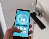 Smartfon z aplikacją do zarządzania domem. Widzimy ikonę otwartej kłódki i przycisk "LOCK". To jest właśnie check in co to.