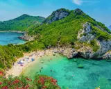 Malownicza zatoka z piaszczystą plażą, turkusową wodą, zielonymi wzgórzami i kwitnącymi kwiatami.
