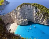 Widok na zatokę Navagio z plażą, klifami i turkusową wodą, z widocznym wrakiem statku.