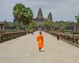 Mnich w pomarańczowej szacie idzie kamienną ścieżką w kierunku Angkor Wat.