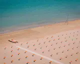 Idealne loty do Rimini: pusta plaża z rzędami parasoli, łódka na piasku i turkusowe morze.