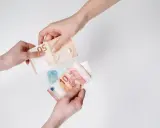 Dwie ręce przekazują sobie banknoty euro. To waluta Słowenii, używana do codziennych zakupów.