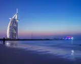 Wieczór w Dubaju. Luksusowy hotel Burdż al-Arab i oświetlony statek na morzu. Ceny w Dubaju mogą być wysokie, ale widoki są niezapomniane.