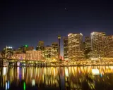 Sydney nocą, z mostem i odbijającymi się w wodzie światłami. Zastanawiasz się, ile się leci do Australii, patrząc na ten widok?