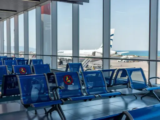 Puste, niebieskie siedzenia na lotnisku w Kalabrii, z widokiem na samolot Aegean i morze.