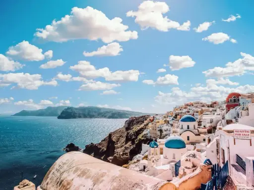 Santorini, Grecja. Białe domy z niebieskimi kopułami kościołów na zboczu góry, nad turkusowym morzem. Marzysz o podróży? Sprawdź, ile się leci do Grecji!