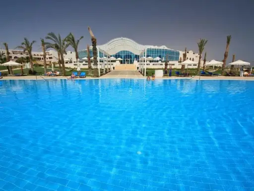 Basen w Hilton Marsa Alam Nubian Resort. Wiele osób odpoczywa na leżakach pod palmami.