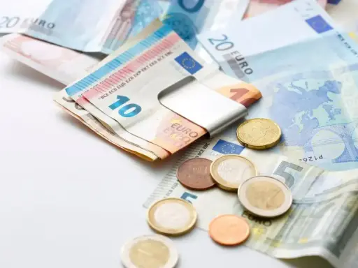 Euro banknoty i monety, czyli waluta w Grecji. Widać banknot 10 euro w metalowym klipsie, a obok monety i banknoty 5, 20 euro.