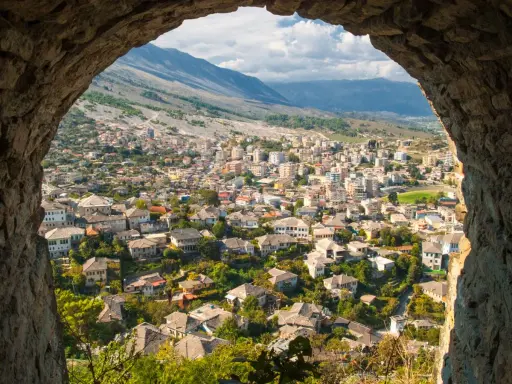 Widok na miasto w Albanii przez kamienny łuk, z górami w tle.