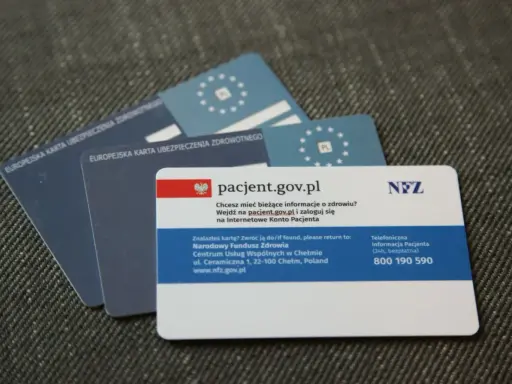 Kilka kart EKUZ i karta pacjenta NFZ na szarym tle.
