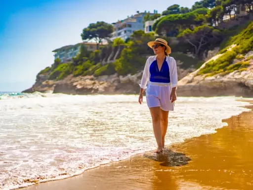 Kobieta w słomkowym kapeluszu spaceruje po plaży. Idealne miejsce na tanie loty na majówkę, by poczuć słońce i fale.