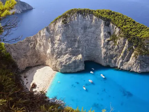 Widok na zatokę Navagio z plażą, klifami i turkusową wodą, z widocznym wrakiem statku.