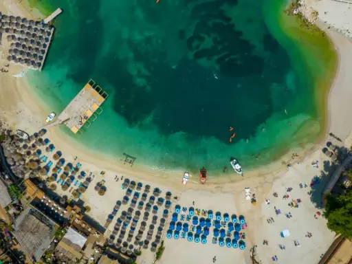 Widok z lotu ptaka na plażę z leżakami, parasolami i turkusową wodą.