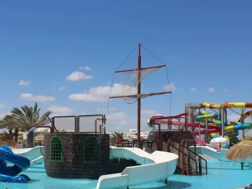 Djerba Aqua Resort (ex. Sun Connect) z pirackim statkiem i kolorowymi zjeżdżalniami wodnymi pod błękitnym niebem.