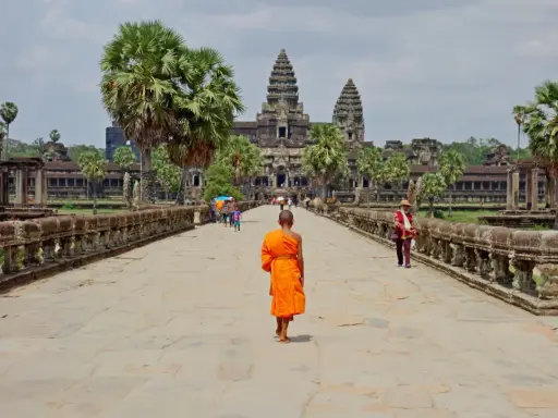 Mnich w pomarańczowej szacie idzie kamienną ścieżką w kierunku Angkor Wat.
