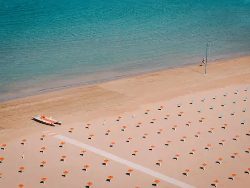 Idealne loty do Rimini: pusta plaża z rzędami parasoli, łódka na piasku i turkusowe morze.