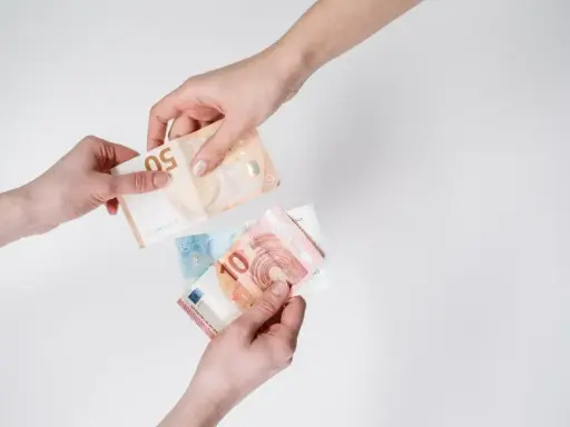 Dwie ręce przekazują sobie banknoty euro. To waluta Słowenii, używana do codziennych zakupów.