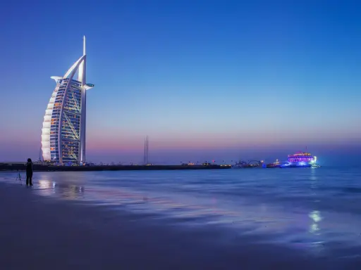 Wieczór w Dubaju. Luksusowy hotel Burdż al-Arab i oświetlony statek na morzu. Ceny w Dubaju mogą być wysokie, ale widoki są niezapomniane.