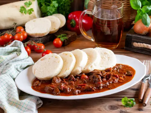 Gulasz z knedlami, piwo i warzywa na drewnianym stole.