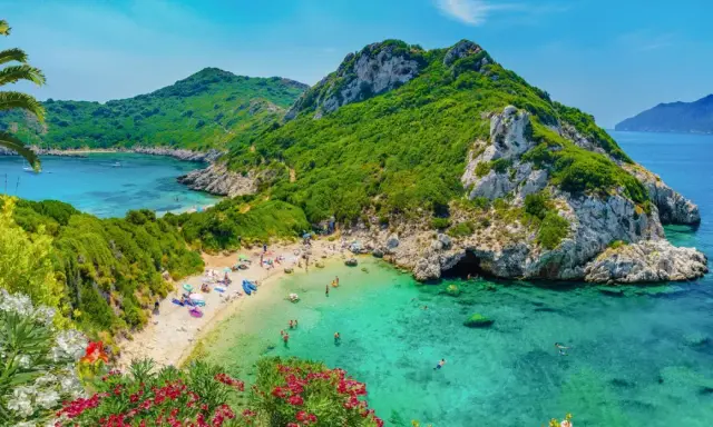 Malownicza zatoka z piaszczystą plażą, turkusową wodą, zielonymi wzgórzami i kwitnącymi kwiatami.