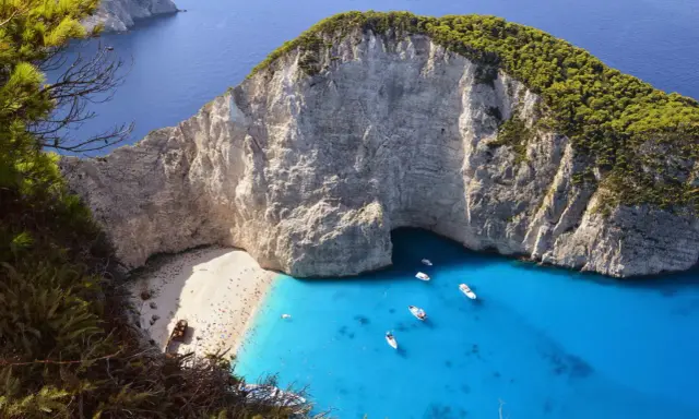 Widok na zatokę Navagio z plażą, klifami i turkusową wodą, z widocznym wrakiem statku.