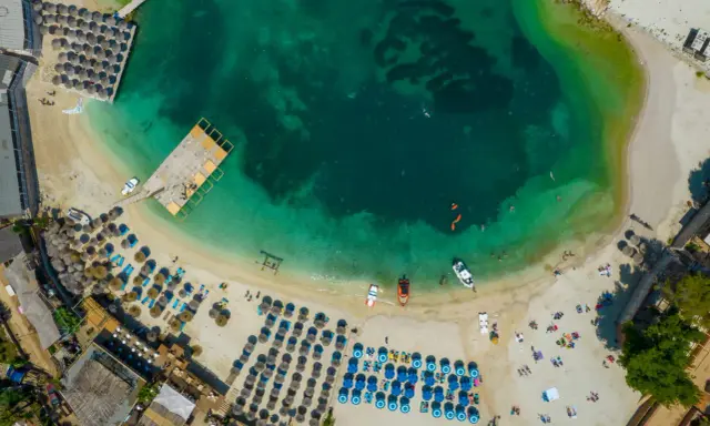 Widok z lotu ptaka na plażę z leżakami, parasolami i turkusową wodą.