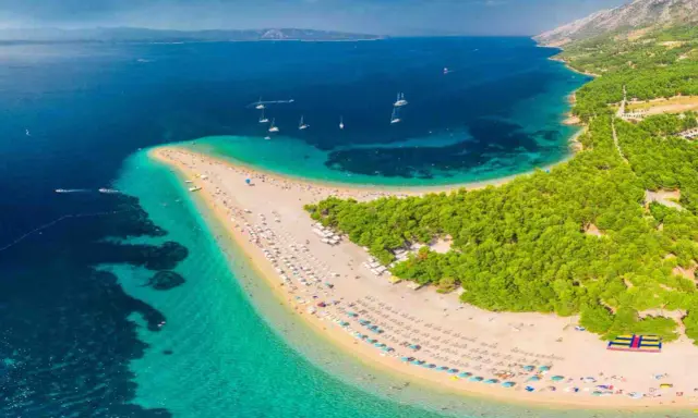 Plaża w kształcie języka, otoczona turkusową wodą i zielonym lasem, z widokiem na góry.