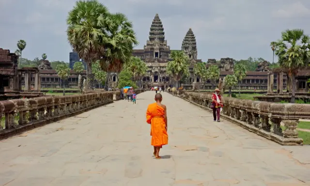 Mnich w pomarańczowej szacie idzie kamienną ścieżką w kierunku Angkor Wat.