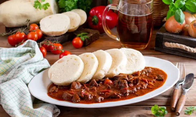 Gulasz z knedlami, piwo i warzywa na drewnianym stole.