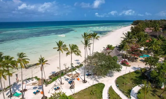 Plaża na Zanzibarze z palmami, turkusową wodą i łodziami.