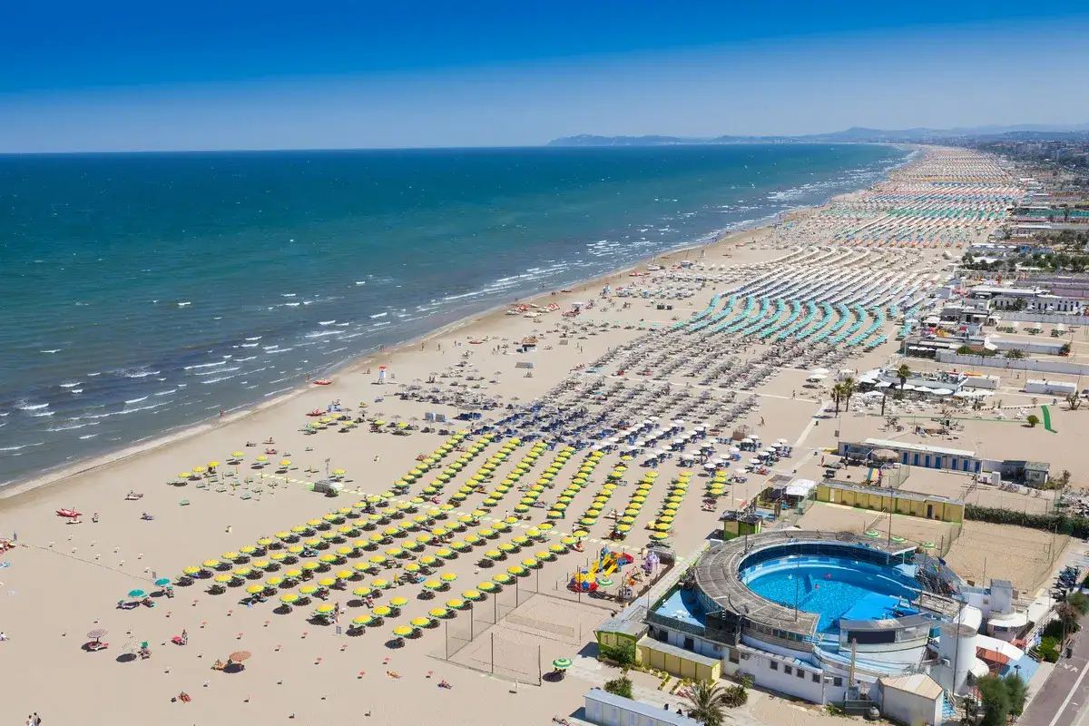Słoneczna plaża w Rimini, pełna leżaków i parasoli, zaprasza na wakacje. Idealne miejsce na loty do Rimini.